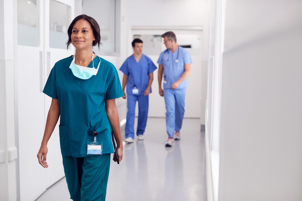 Female,Doctor,Wearing,Scrubs,In,Hospital,Walking,Along,Corridor,Holding